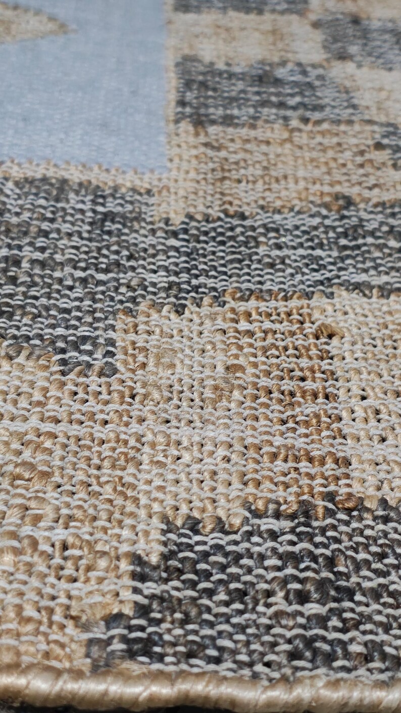 May include: A woven area rug featuring a checkered pattern composed of alternating squares in natural tan jute and dark charcoal gray fibers. The textile has a thick, textured weave with a visible grid structure and a finished bound edge.