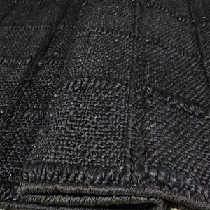 Puede incluir: Primer plano de una alfombra negra tejida con un patr&oacute;n geom&eacute;trico en forma de cuadr&iacute;cula. La alfombra tiene una superficie texturizada y un color oscuro, carb&oacute;n. Los bordes est&aacute;n cuidadosamente acabados con un borde tejido. Esta alfombra es adecuada para la decoraci&oacute;n del hogar.