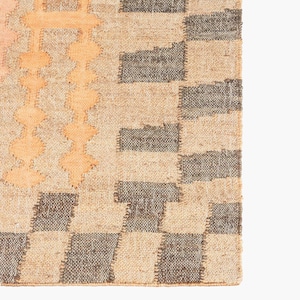 Op de afbeelding: Een close-up van een geweven tapijt met een geometrisch patroon. Het tapijt is gemaakt van natuurlijke vezels en heeft een beige en bruine kleurstelling.