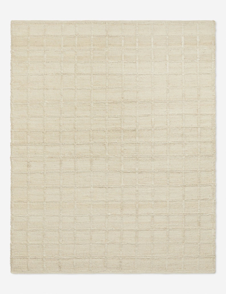 May include: A rectangular area rug in a solid cream color featuring a woven grid pattern. The surface is composed of a series of raised, horizontal and vertical lines that intersect to form uniform squares across the entire textile construction.