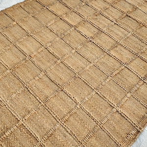 May include: A rectangular area rug crafted from natural tan fibers, featuring a prominent grid pattern created by raised, woven lines that intersect to form uniform squares across the entire surface of the textured floor covering.