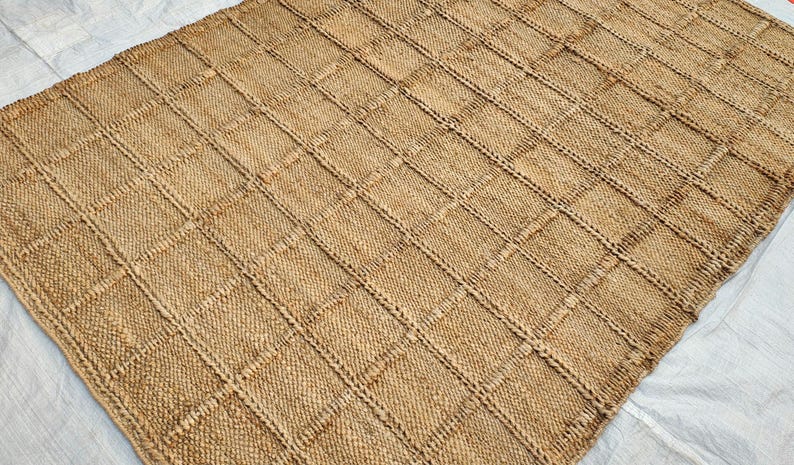 May include: A rectangular area rug crafted from natural tan fibers, featuring a prominent grid pattern created by raised, woven lines that intersect to form uniform squares across the entire surface of the textured floor covering.