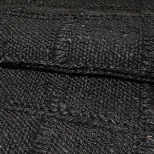 Puede incluir: Primer plano de una alfombra tejida de color gris oscuro con una superficie texturizada. La alfombra tiene un patr&oacute;n geom&eacute;trico con secciones elevadas y un brillo sutil. El material parece ser una fibra natural, posiblemente yute o similar.