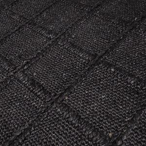 May include: A rectangular area rug featuring a dark black color and a woven texture. The rug is constructed with a grid pattern of square sections, each defined by thick, braided borders that create a raised, tactile surface across the entire piece.