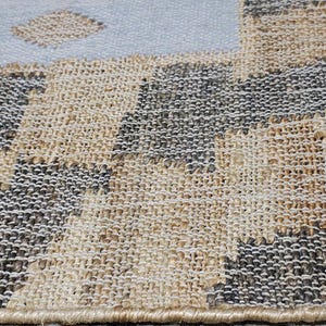 May include: A woven area rug featuring a textured checkerboard pattern in alternating squares of natural tan and dark charcoal gray. The rug has a finished bound edge and transitions into a solid light blue section with small tan diamond shapes.