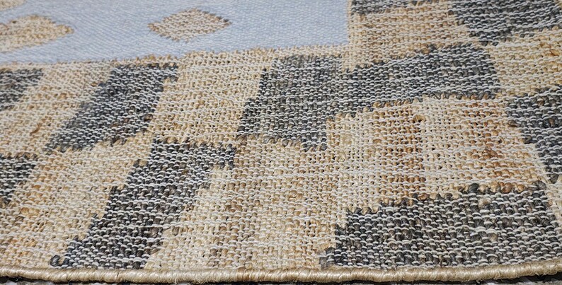 May include: A woven area rug featuring a textured checkerboard pattern in alternating squares of natural tan and dark charcoal gray. The rug has a finished bound edge and transitions into a solid light blue section with small tan diamond shapes.