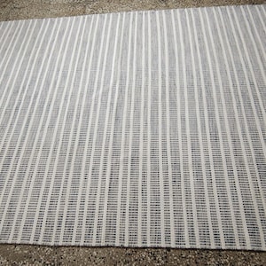 May include: A rectangular area rug featuring a repeating pattern of thin, vertical stripes in alternating shades of dark navy blue and off-white. The woven textile displays a consistent linear design across its entire surface, creating a textured appearance.