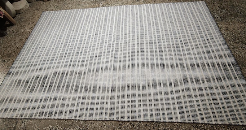 May include: A rectangular area rug featuring a repeating pattern of thin, vertical stripes in alternating shades of dark navy blue and off-white. The woven textile displays a consistent linear design across its entire surface, creating a textured appearance.