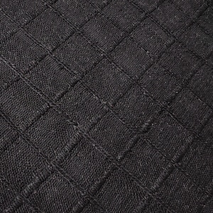 May include: A round, black area rug featuring a textured, woven surface with a prominent grid pattern formed by raised lines. The rug has a consistent dark charcoal tone and a dense, fibrous construction that creates a uniform, geometric appearance.