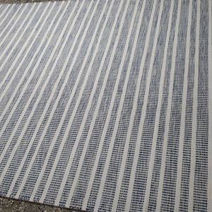 May include: A rectangular area rug featuring a repeating pattern of vertical stripes in dark blue and off-white. The design consists of alternating thin and thick lines, creating a textured appearance across the entire surface of the woven floor covering.