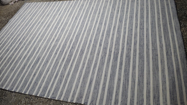 May include: A rectangular area rug featuring a repeating pattern of vertical stripes in dark blue and off-white. The design consists of alternating thin and thick lines, creating a textured appearance across the entire surface of the woven floor covering.
