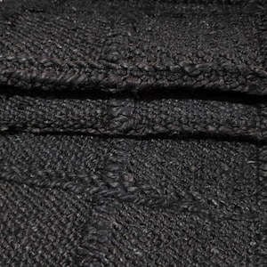 Puede incluir: Primer plano de un textil tejido plegado de color carb&oacute;n oscuro. La tela tiene una apariencia texturizada y nudosa con costuras visibles y un patr&oacute;n sutil. El material parece grueso y duradero.