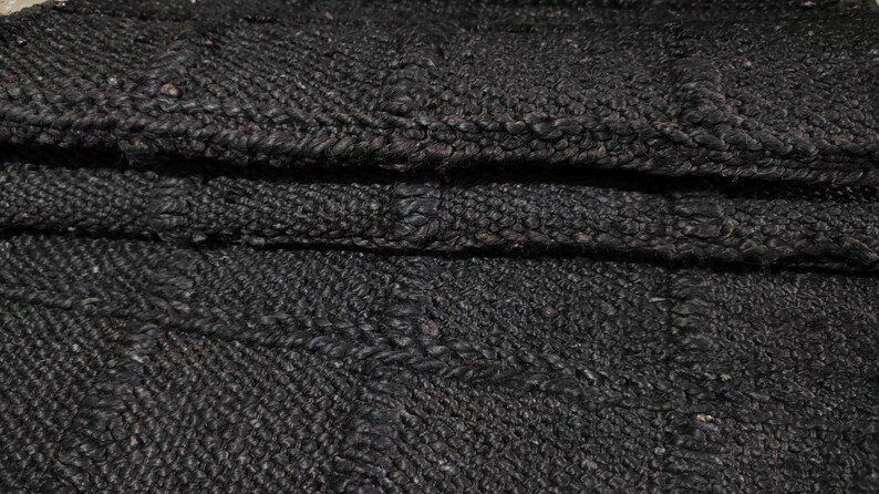 Puede incluir: Primer plano de un textil tejido plegado de color carb&oacute;n oscuro. La tela tiene una apariencia texturizada y nudosa con costuras visibles y un patr&oacute;n sutil. El material parece grueso y duradero.
