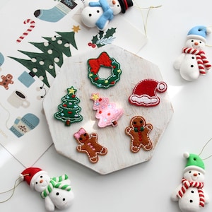 May include: A selection of Christmas decorations and stickers. The ornaments include a green wreath with a red bow, a red Santa hat, and gingerbread people. The stickers feature a Christmas tree, a snowman, and other festive designs.
