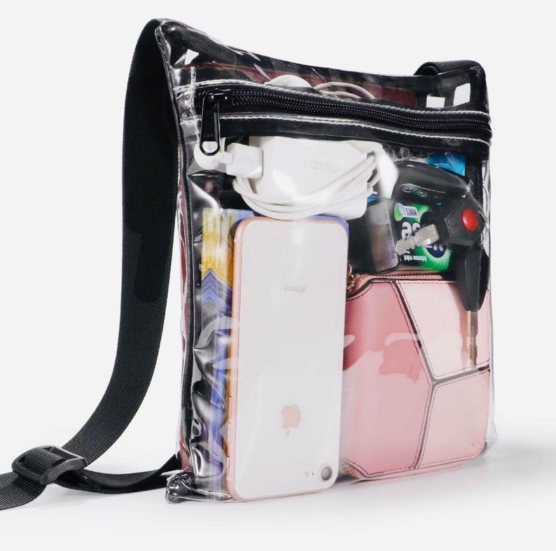 Peut inclure: Sac bandouli&egrave;re transparent avec une bandouli&egrave;re et une fermeture &eacute;clair noires. Le sac contient un smartphone blanc, un sac &agrave; main rose, un chargeur blanc et d'autres articles. Le sac est con&ccedil;u pour &ecirc;tre transparent, permettant une visibilit&eacute; facile du contenu.