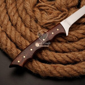 May include: A close-up of a brown wooden handled knife with a stainless steel blade. The knife is resting on a thick brown rope.