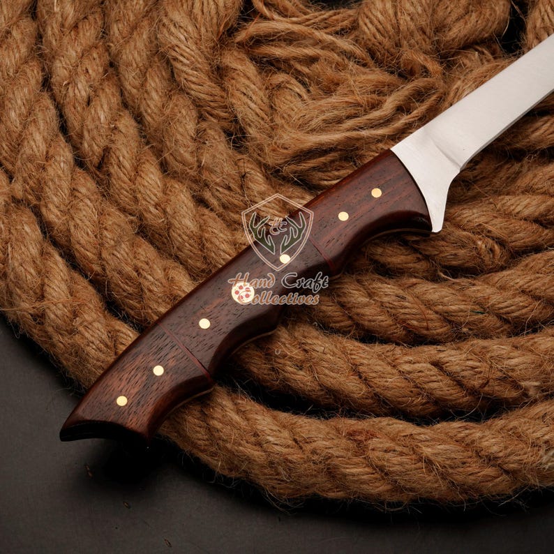 May include: A close-up of a brown wooden handled knife with a stainless steel blade. The knife is resting on a thick brown rope.