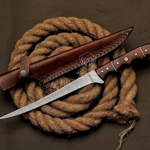 May include: A Damascus steel fishing knife with a brown wooden handle and a leather sheath. The knife is lying on a coil of brown rope.