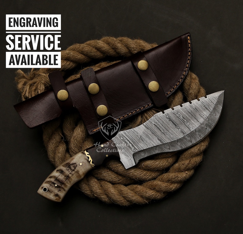 May include: A Damascus steel knife with a brown leather sheath. The knife has a patterned blade and a bone handle. The sheath is secured with brass-colored studs. Text on the image reads "ENGRAVING SERVICE AVAILABLE."