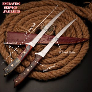May include: Two knives with wooden handles and silver blades. The knife on the left has a Pakkawood handle with red and black accents. The knife on the right has a Rose Wood handle. The blades are 13 inches long and made of J2 steel. The knives are displayed on a brown rope background. Engraving service available.