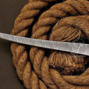 May include: A curved, silver-colored knife with a wooden handle and a patterned blade. The knife is resting on a brown rope.