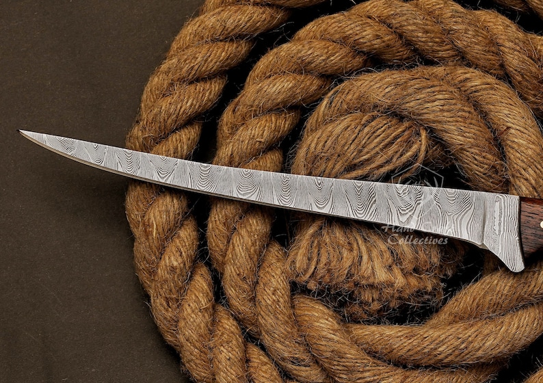 May include: A curved, silver-colored knife with a wooden handle and a patterned blade. The knife is resting on a brown rope.
