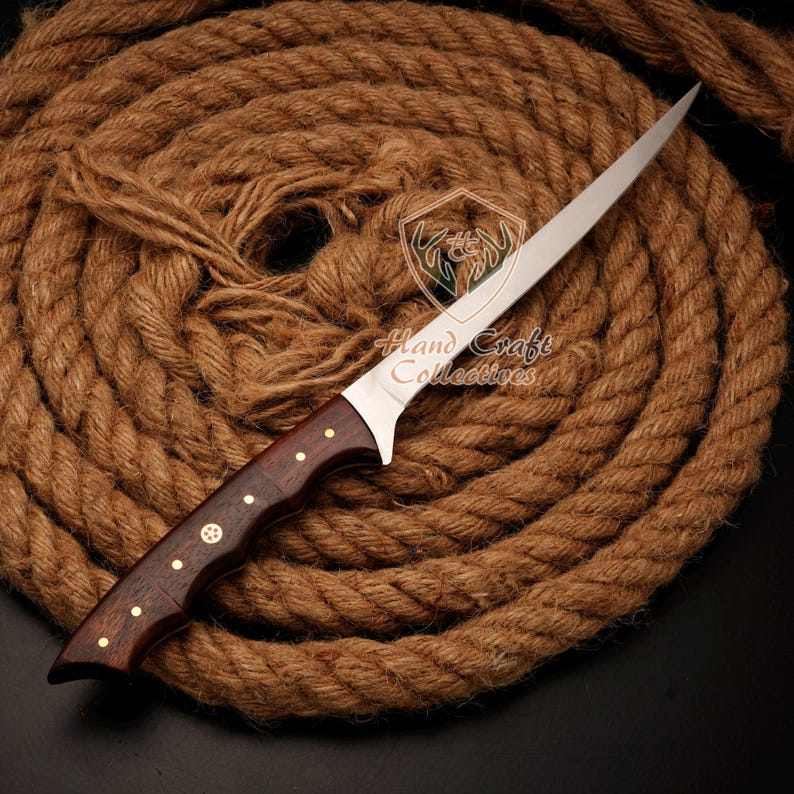 May include: A long, thin, silver knife with a brown wooden handle. The handle has brass accents and a decorative star design. The knife is lying on a coil of brown rope.