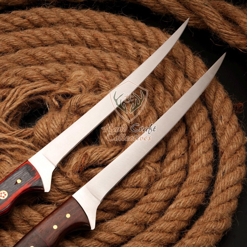 May include: Two long, thin, silver-colored knives with wooden handles. The handles are a dark brown wood with red and gold accents. The knives are lying on a brown rope background.