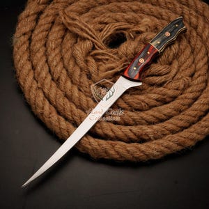 May include: A long, thin, silver knife with a black and red wooden handle. The knife is lying on a coil of brown rope.