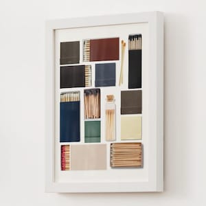 May include: A framed collage of various matchboxes and matchsticks. The matchboxes are in different colors and patterns, including red, brown, blue, green, and black. Some of the matchboxes are filled with matches, while others are empty. The matchsticks are arranged in a variety of ways, some are in bundles, some are loose, and some are in a small glass bottle.