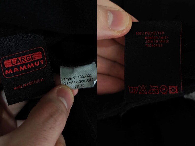 Puede incluir: Primer plano de tela negra con varias etiquetas. Una etiqueta presenta el texto rojo "LARGE MAMMUT" y "MADE IN PORTUGAL". Otra etiqueta muestra "Style N. 1030031" y "Serial N.:3001044". Una tercera tiene instrucciones de lavado y el texto "100% POLYESTER".