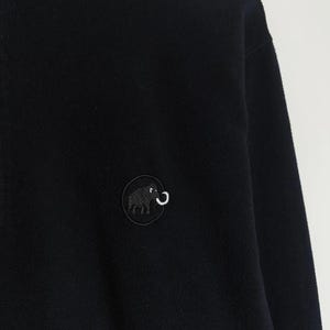 Puede incluir: Chaqueta polar negra con un parche redondo que presenta un elefante negro y un colmillo blanco curvado. La chaqueta tiene un aspecto suave y texturizado y un dise&ntilde;o sencillo. El parche est&aacute; bordado con finos detalles.