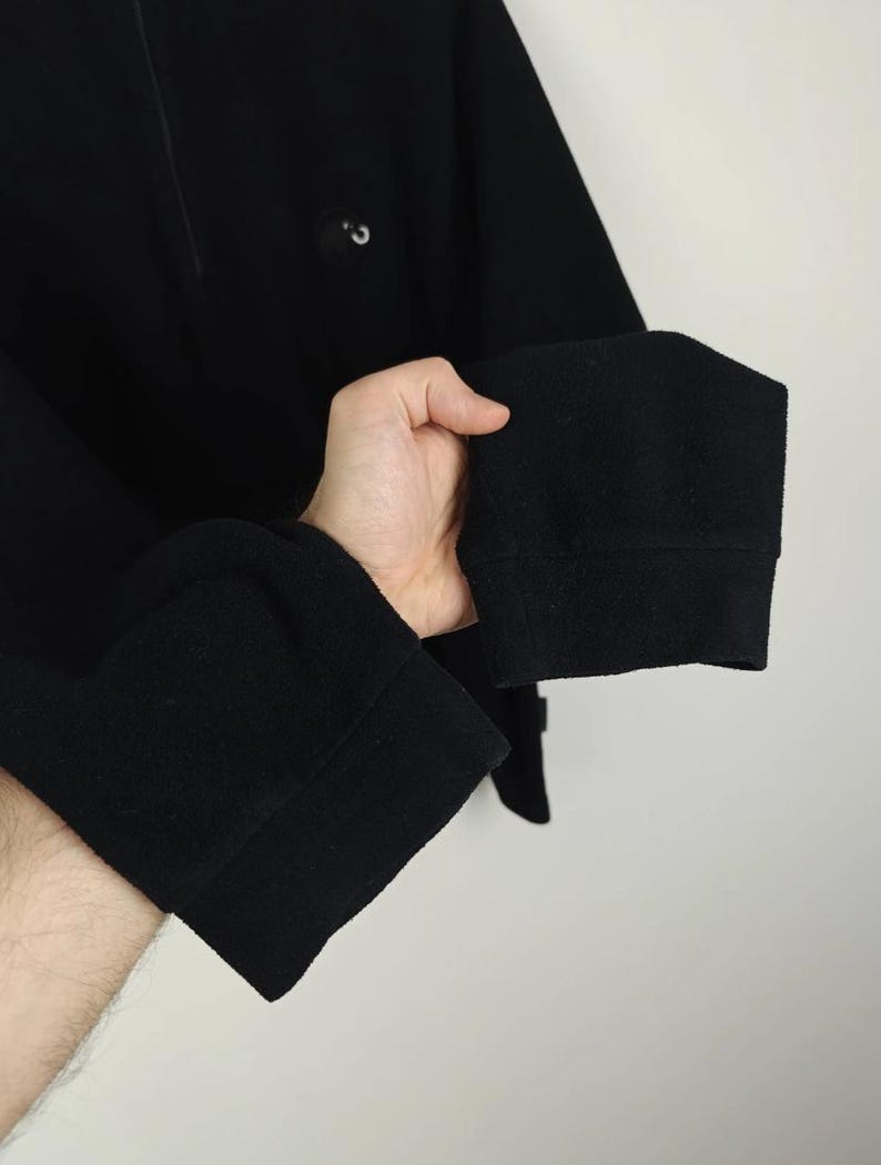 Puede incluir: Camisa negra de manga larga con cuello alto y un peque&ntilde;o detalle de bot&oacute;n. Los pu&ntilde;os son gruesos y doblados. La camisa est&aacute; hecha de una tela suave y texturizada.
