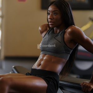 May include: A woman with long black hair is doing a tricep dip exercise on a weight bench at the gym. She is wearing a gray sports bra and black shorts. Her abs are visible.
