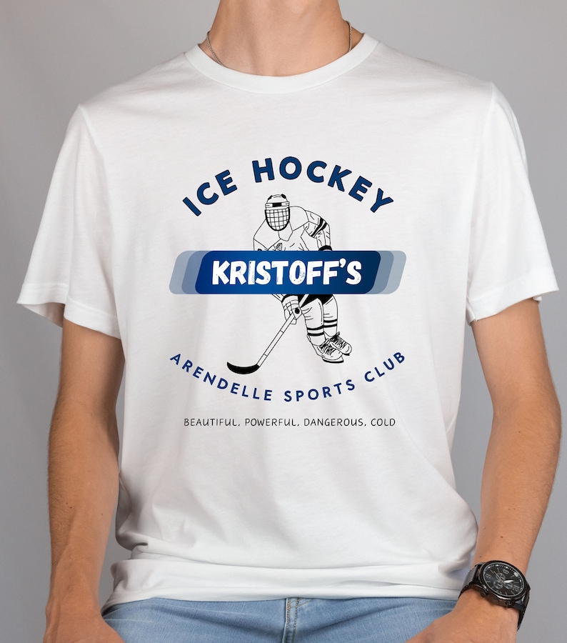 May include: White t-shirt with a blue and white graphic of an ice hockey player. The graphic says "Ice Hockey Kristoff's Arendelle Sports Club" and "Beautiful. Powerful. Dangerous. Cold."
