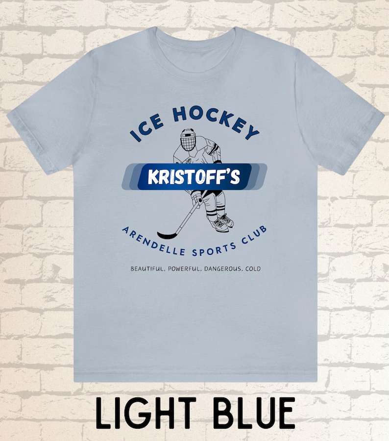 May include: Light blue t-shirt with a graphic of an ice hockey player and the text "ICE HOCKEY KRISTOFF'S ARENDELLE SPORTS CLUB BEAUTIFUL, POWERFUL, DANGEROUS, COLD"