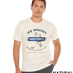 May include: White t-shirt with a blue graphic of an ice hockey player. The graphic says "ICE HOCKEY KRISTOFF'S ARENDELLE SPORTS CLUB BEAUTIFUL. POWERFUL. DANGEROUS. COLD."