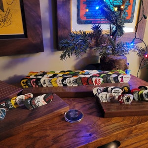 May include: Two wooden guitar pick holders with a variety of colorful guitar picks. The holders are on a wooden surface.