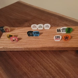 May include: A wooden guitar pick holder with a variety of guitar picks, including picks with the names "Lauren Alaina", "Fire from the Gods", "Sonic Warriors", and "The Crown".