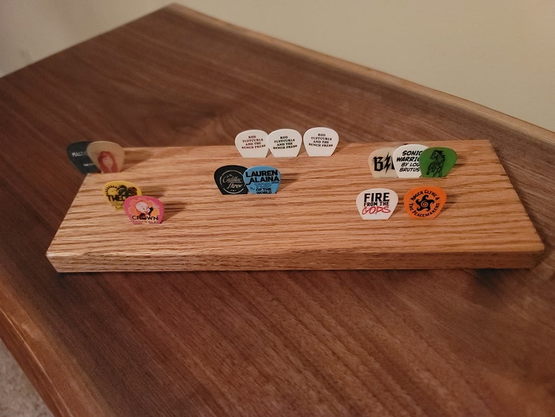 May include: A wooden guitar pick holder with a variety of guitar picks, including picks with the names "Lauren Alaina", "Fire from the Gods", "Sonic Warriors", and "The Crown".