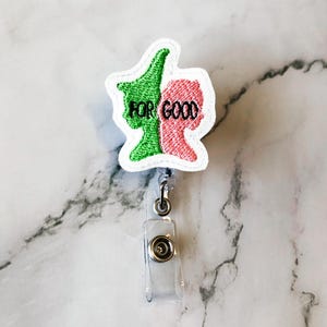 May include: A badge reel with a white border featuring two side profiles, one green and one pink, with the words "FOR GOOD" embroidered in black. The reel has a clear plastic strap and a metal clip.