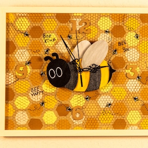 May include: A wooden bee clock with black and yellow stripes, set against a honeycomb background. The clock face features the numbers 12, 9, 6, and 3. The bee has black eyes and the words "Bee Happy", "Bee Kind", and "Bee You" are written on the honeycomb.