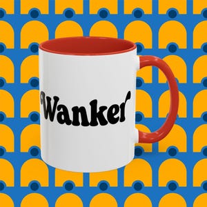 May include: White coffee mug with a red rim and handle. The mug has the word "Wanker" printed in black on the front.