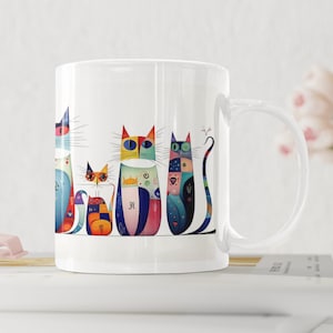 May include: White ceramic mug featuring a colourful illustration of five cats. The cats are all different colours and patterns, and they are arranged in a row. The mug has a handle on the right side.