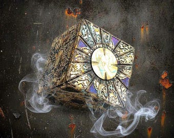 May include: A decorative puzzle box featuring a complex gold and black geometric pattern with intricate engravings and a central circular gold disc on each face, surrounded by wisps of white smoke against a dark, weathered, rusted metal background.