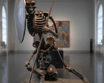 May include: Bronze sculpture of a skeleton warrior holding a spear and shield. The skeleton is posed in a dynamic stance, atop a base with additional skulls. The sculpture is displayed in a museum setting, behind glass.