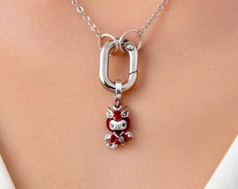 May include: A silver-toned chain necklace featuring a large oval carabiner-style clasp. Attached to the clasp is a small, detailed pendant shaped like a stylized creature with bright red enamel accents and silver-toned metal detailing.