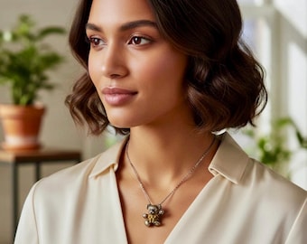 May include: A silver necklace with a small teddy bear pendant. The teddy bear has a gold heart on its chest and is wearing a small bow. The woman is wearing a cream-colored blouse.