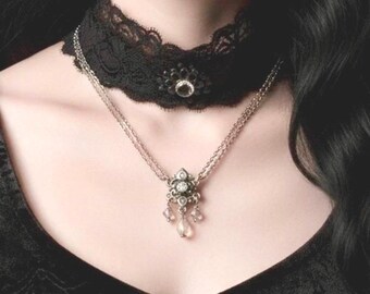 May include: A black lace choker necklace with a central decorative element and a silver chain necklace with a pendant featuring clear gemstones. The jewelry is set against a dark background.