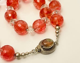 May include: A necklace made of faceted red and clear beads with a silver clasp featuring a green and brown stone.